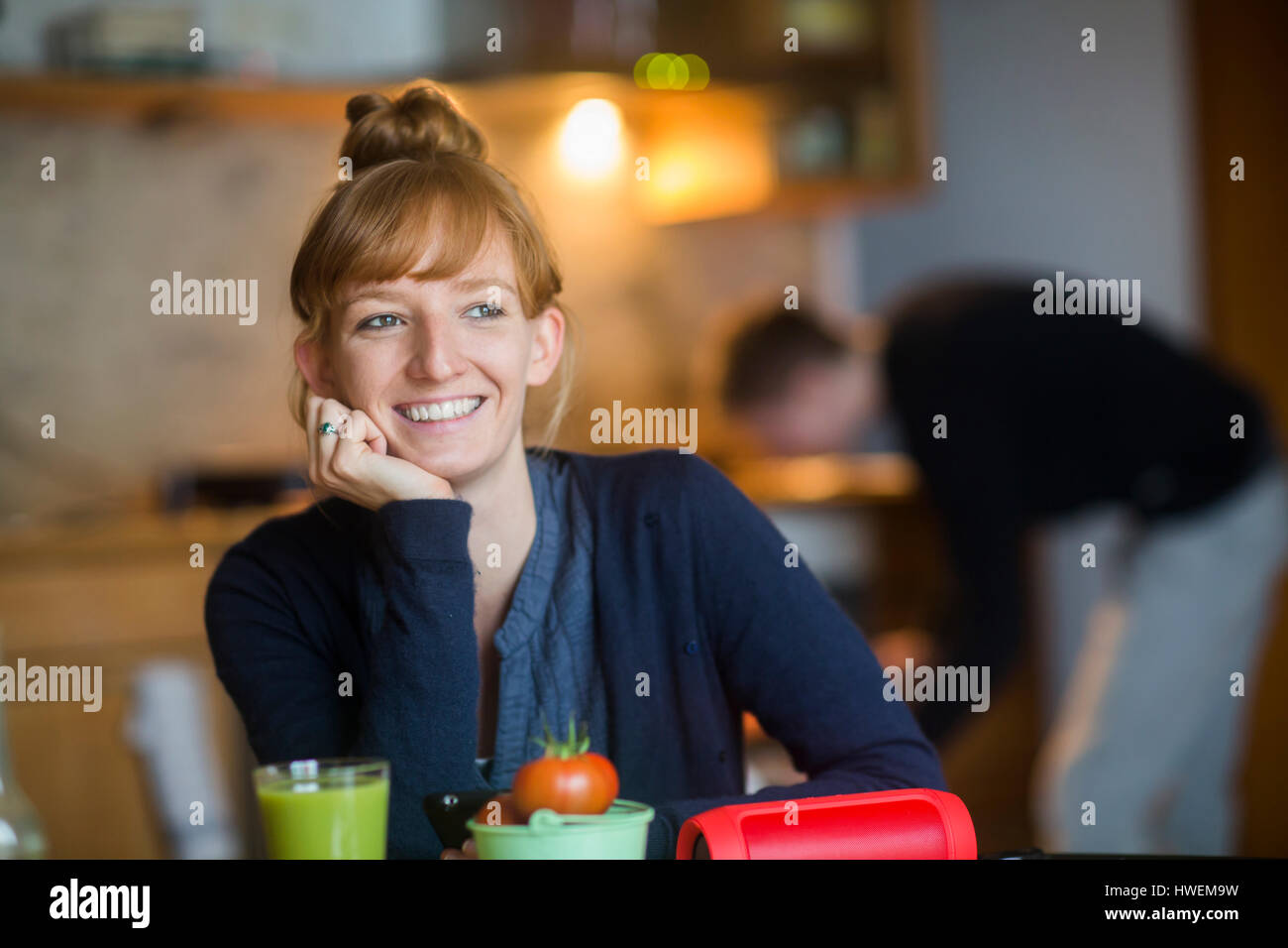 Porträt der jungen Frau, sitzt am Tisch, Smoothie auf Tisch vor ihr Stockfoto