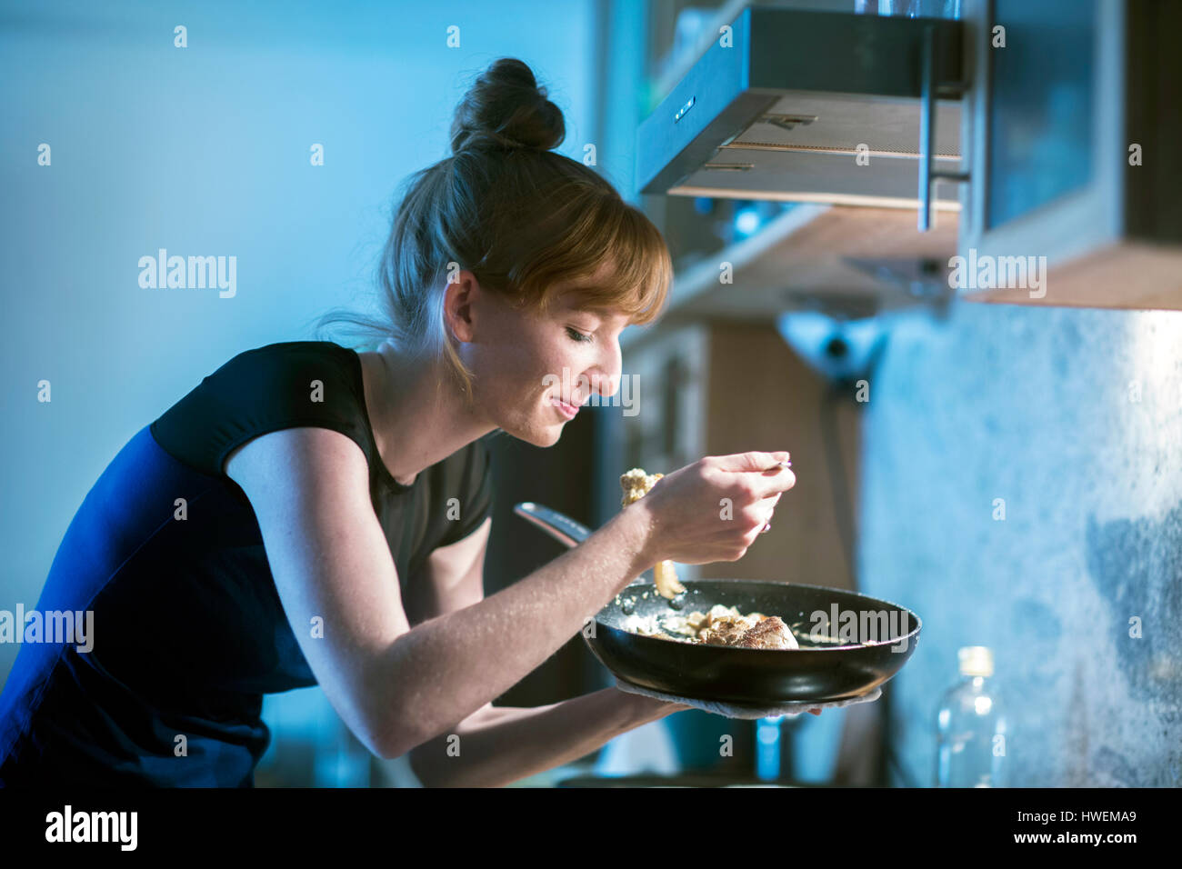 Junge Frau schmeckendes Essen aus der Pfanne Stockfoto