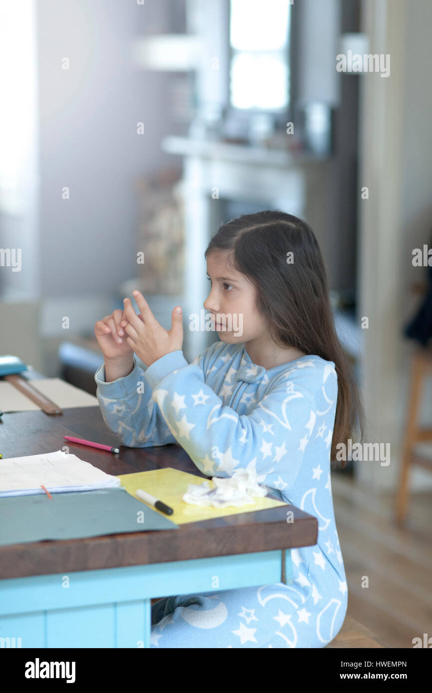 Mädchen, Hausaufgaben und zählt an den Fingern am Küchentisch Stockfoto