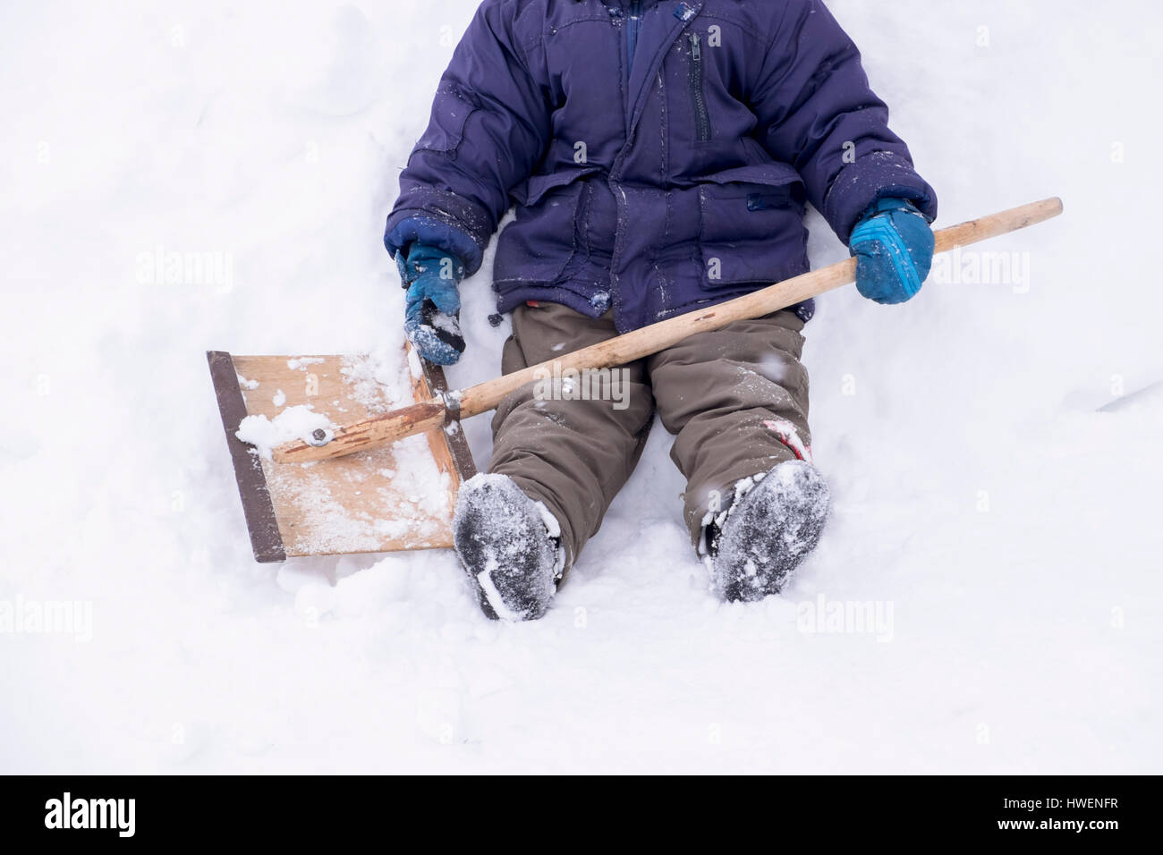 Baby Junge sitzt auf Schnee mit Schaufel Stockfoto