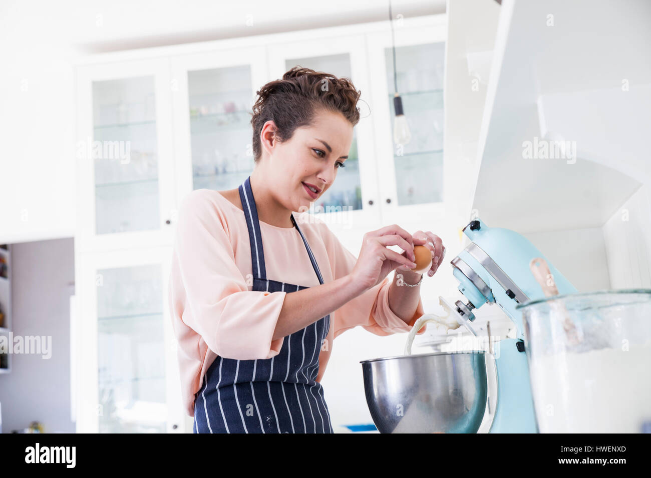 Junge Frau knacken Ei in Mixer Futternapf am Küchentisch Stockfoto