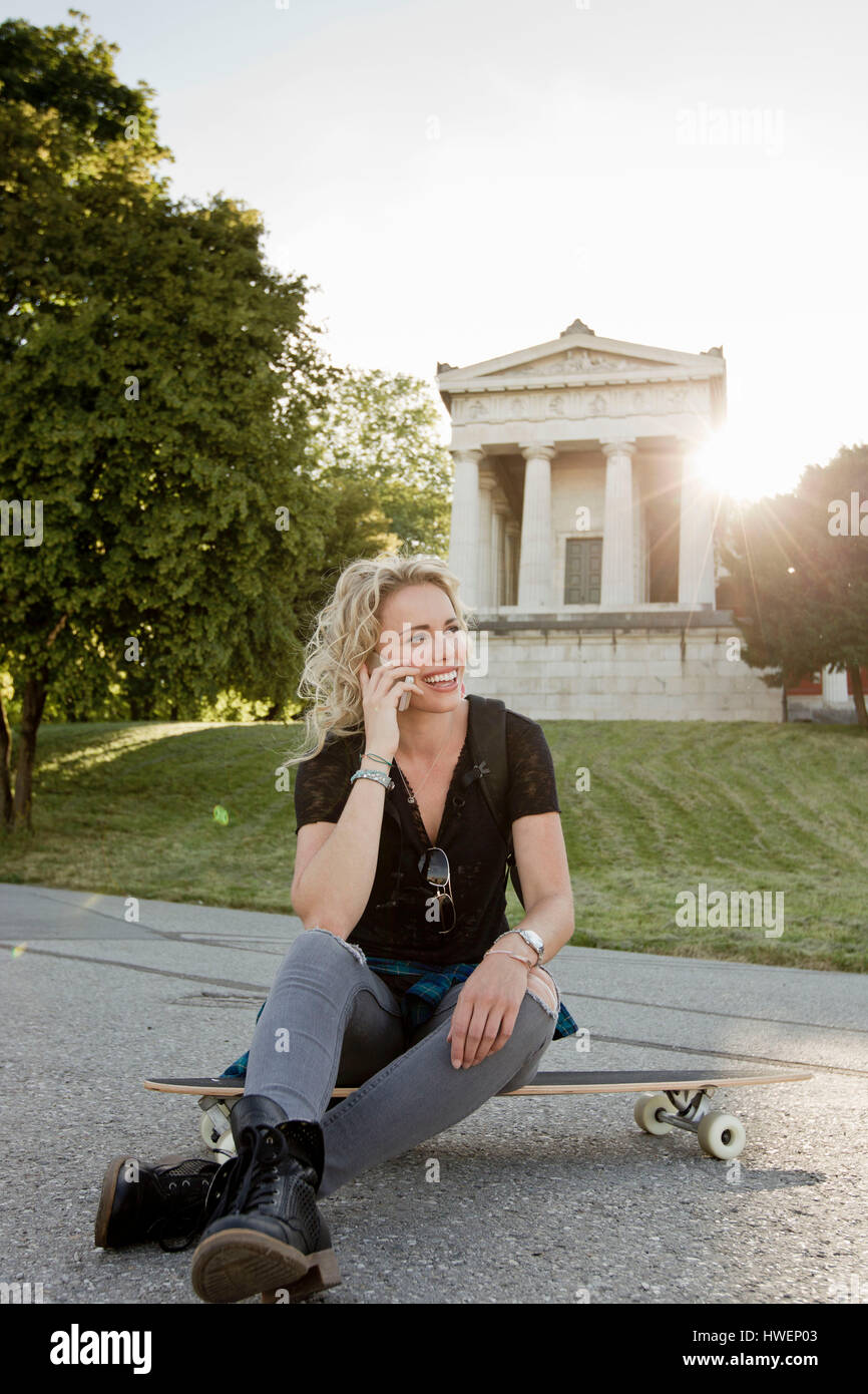 Weibliche Skateboarder sitzen auf Skateboard Park Smartphone Anruf tätigen Stockfoto