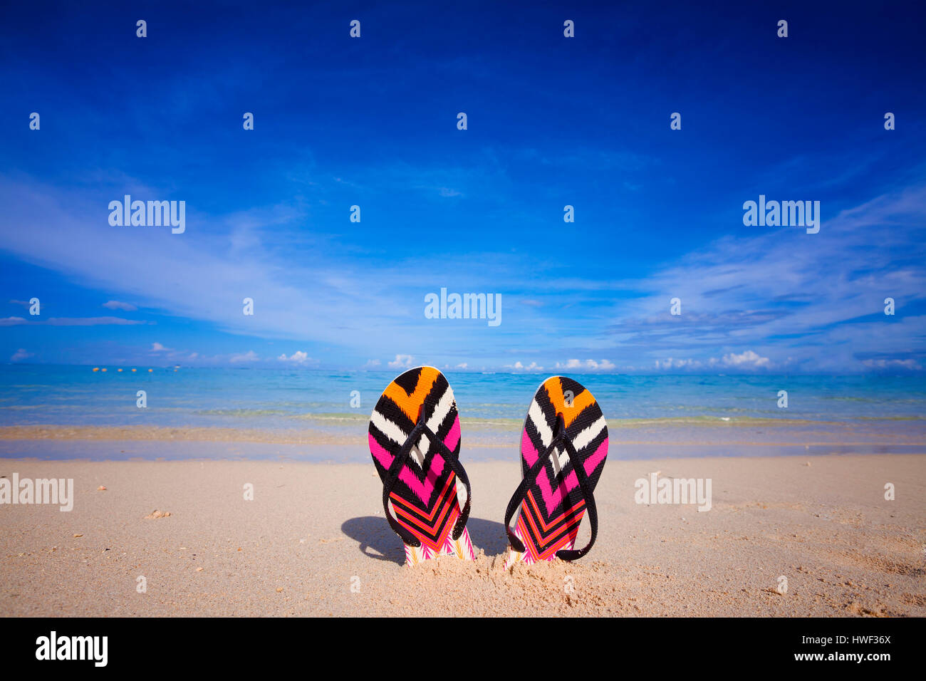 Bunte Flip-flops stecken in den Sand am tropischen Strand mit türkisfarbenem Meer im Hintergrund Stockfoto