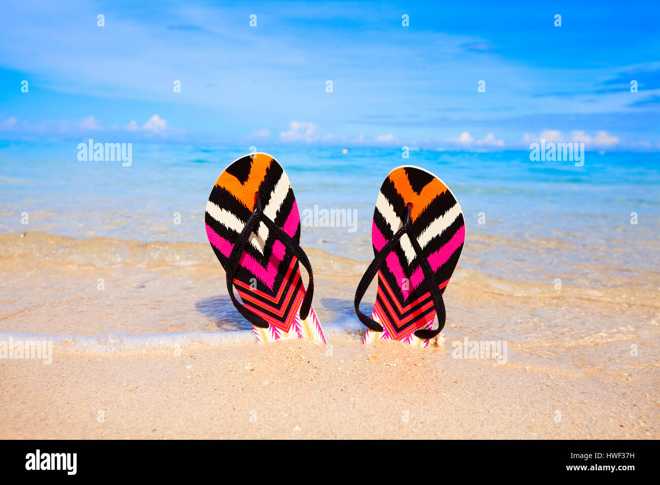 Bunte Flip-flops stecken in den Sand am tropischen Strand mit türkisfarbenem Meer im Hintergrund Stockfoto