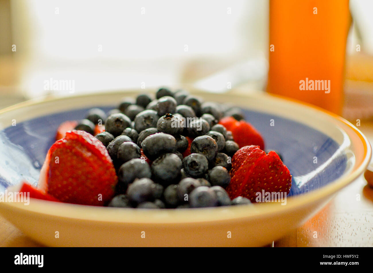 Die Heidelbeeren werden gewaschen und die Erdbeeren geschnitten worden. Sie sind in einer blauen Schüssel mit einem hellen Hintergrund. Stockfoto