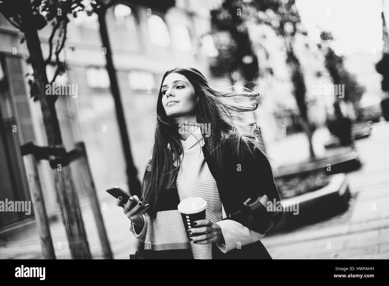 Blick auf junge Frau draußen, trinken Kaffee zum mitnehmen und hält ein Handy in der hand Stockfoto