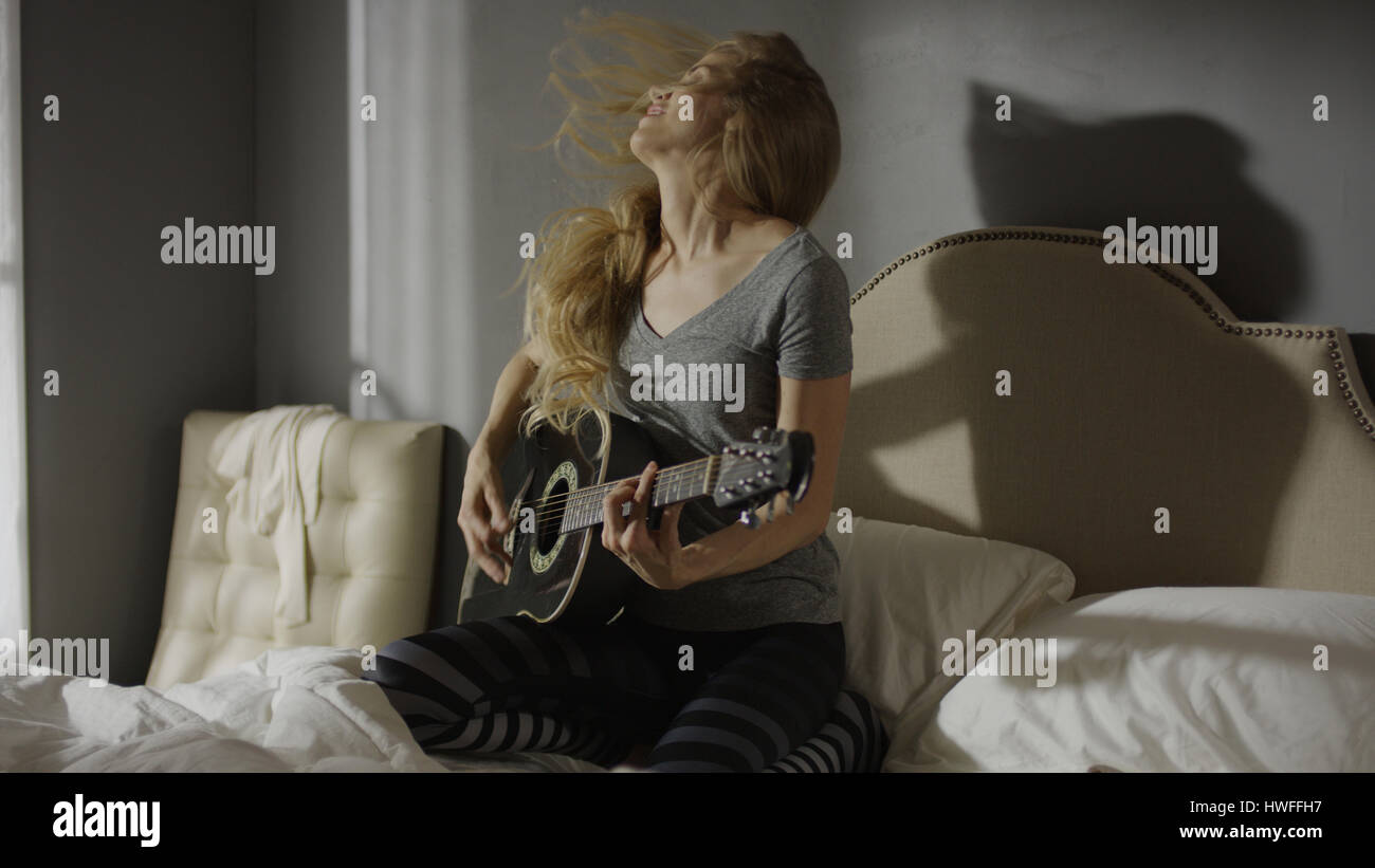 Intensive Musiker wirft Haar und spielte Gitarre auf Bett Stockfoto