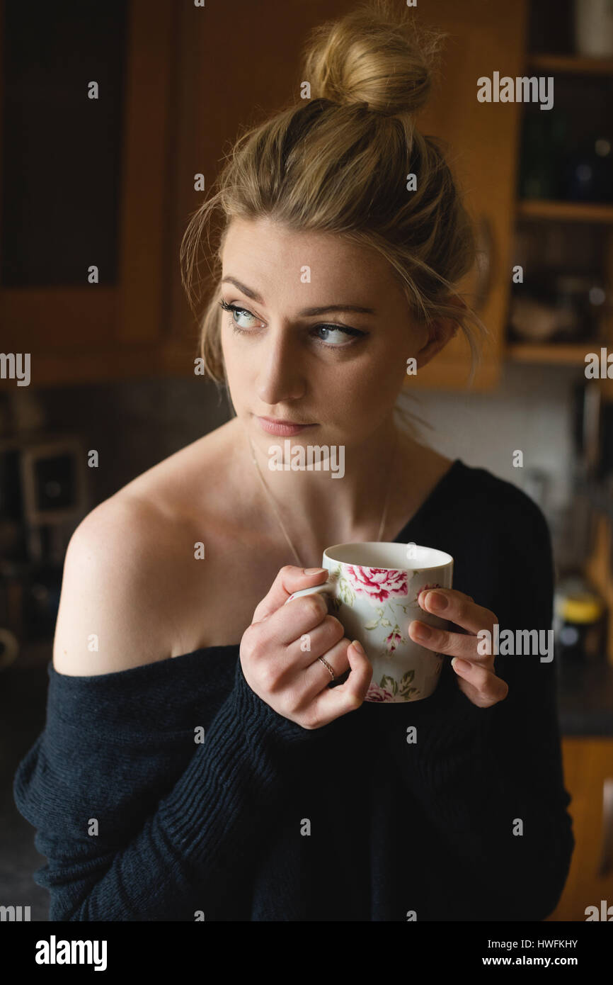 Nachdenkliche Frau hält eine Kaffeetasse in der Küche zu Hause Stockfoto