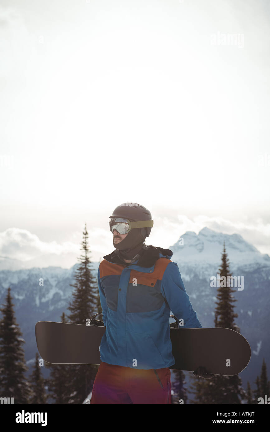 Mann hält Snowboard gegen schneebedeckten Berg Stockfoto