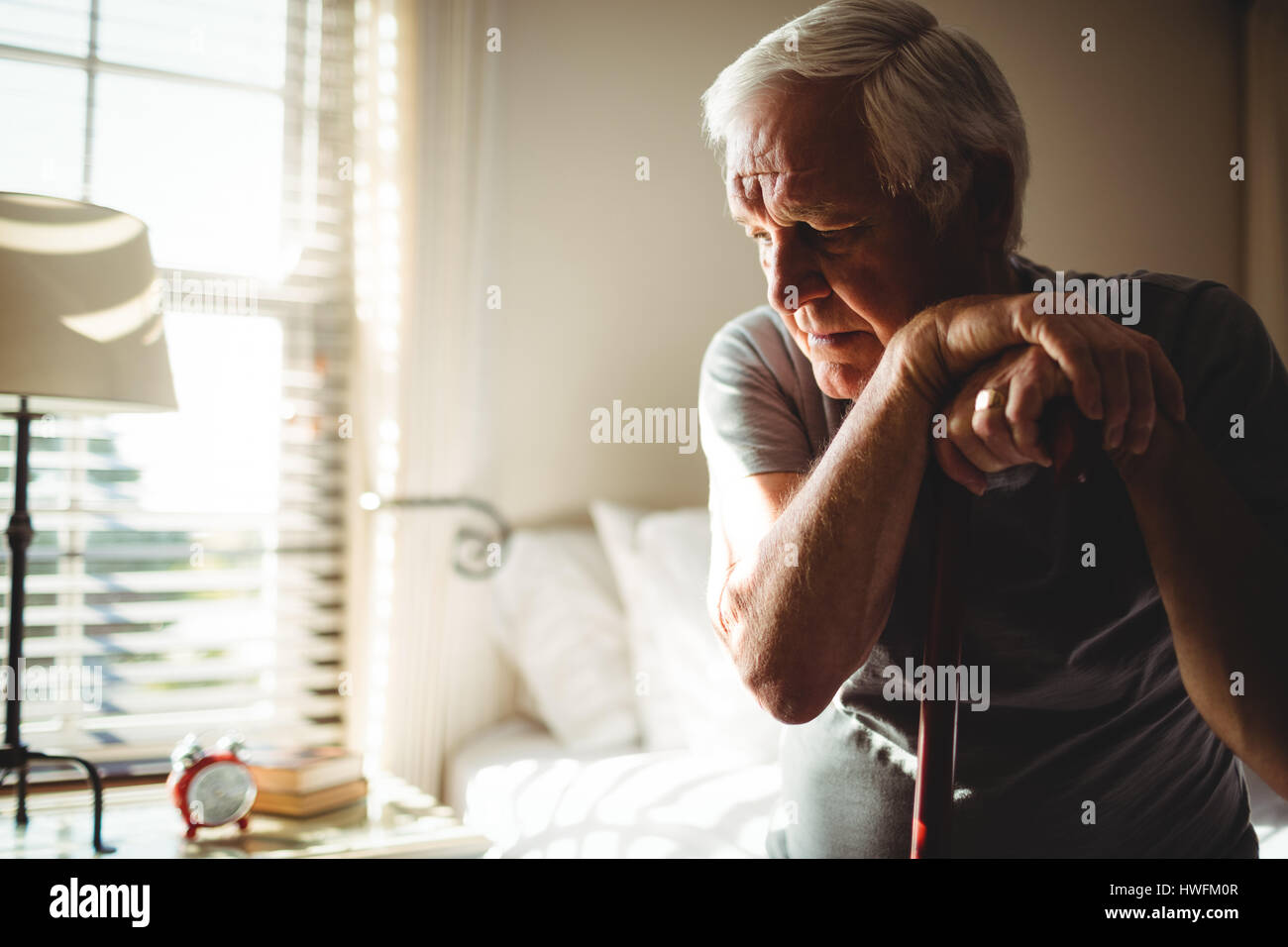 Nachdenklicher senior Mann mit seinem Gehstock im Schlafzimmer zu Hause Stockfoto