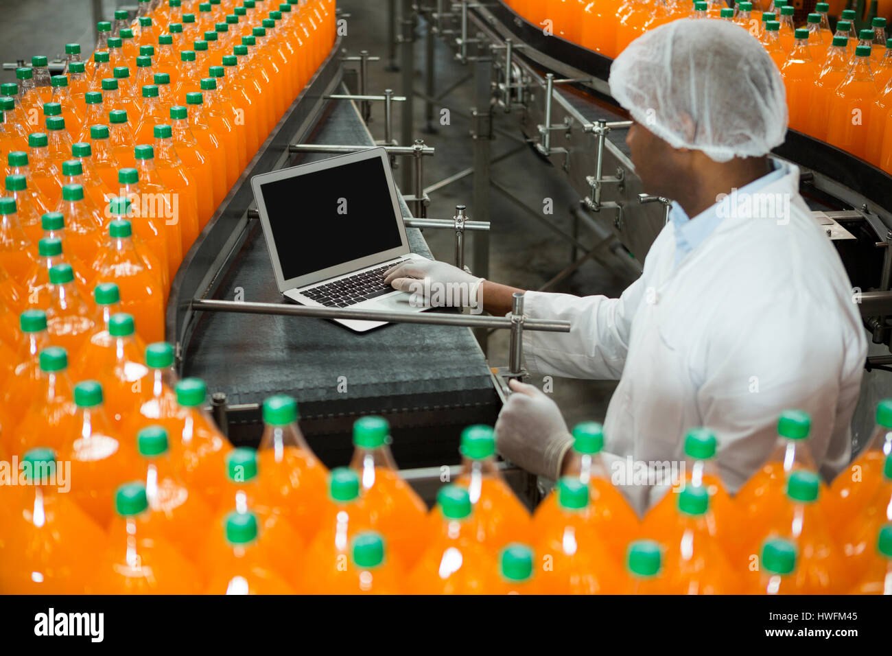 Erhöhte Ansicht der männlichen Arbeitnehmer mit Laptop inmitten Produktionslinie in Fruchtsaft Fabrik Stockfoto