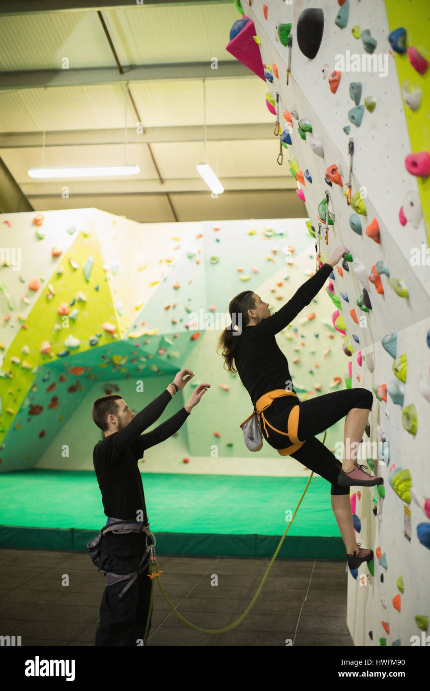 Trainer unterstützen Frau beim Klettern an künstlichen Wand im Fitness-Studio Stockfoto
