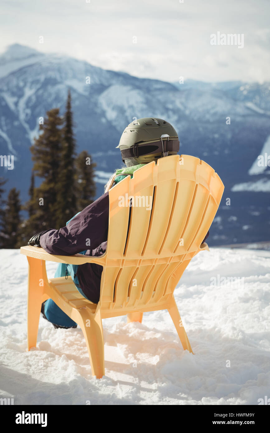 Rückansicht des Frau sitzend auf Stuhl bei Schnee Berg gegen Himmel bedeckt Stockfoto