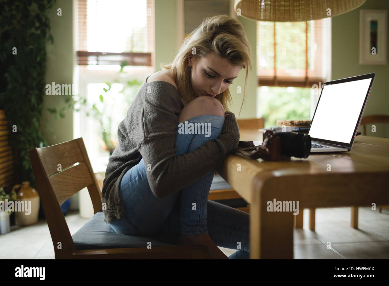 Nachdenkliche Frau mit Laptop zu Hause sitzen Stockfoto