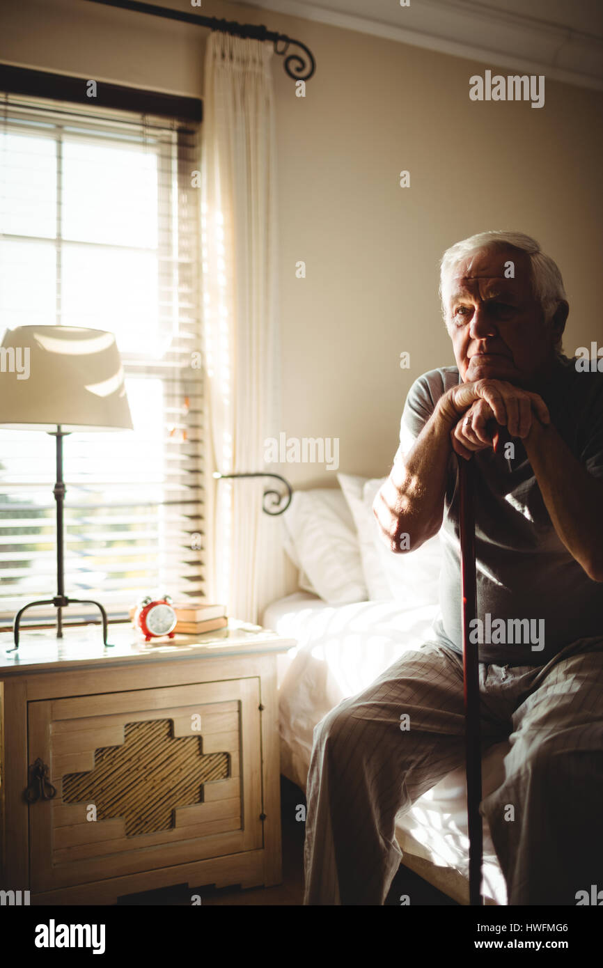 Nachdenklicher senior Mann mit seinem Gehstock im Schlafzimmer zu Hause Stockfoto