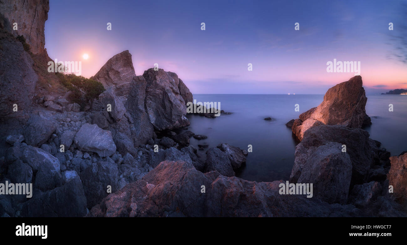 Majestätische hohe Felsen und Steinen Glühen bei Mondschein auf dem See. Fantastische Nacht Panorama-Landschaft mit Bergen, Vollmond, lila leuchtenden Sternenhimmel sk Stockfoto