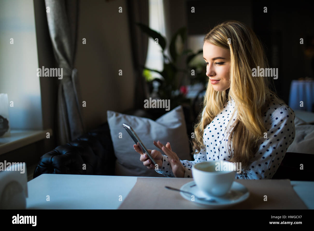 Charmante Frau mit schönen Lächeln gute Nachrichten auf dem Handy zu lesen, während der Rest in Coffee-Shop, Stockfoto