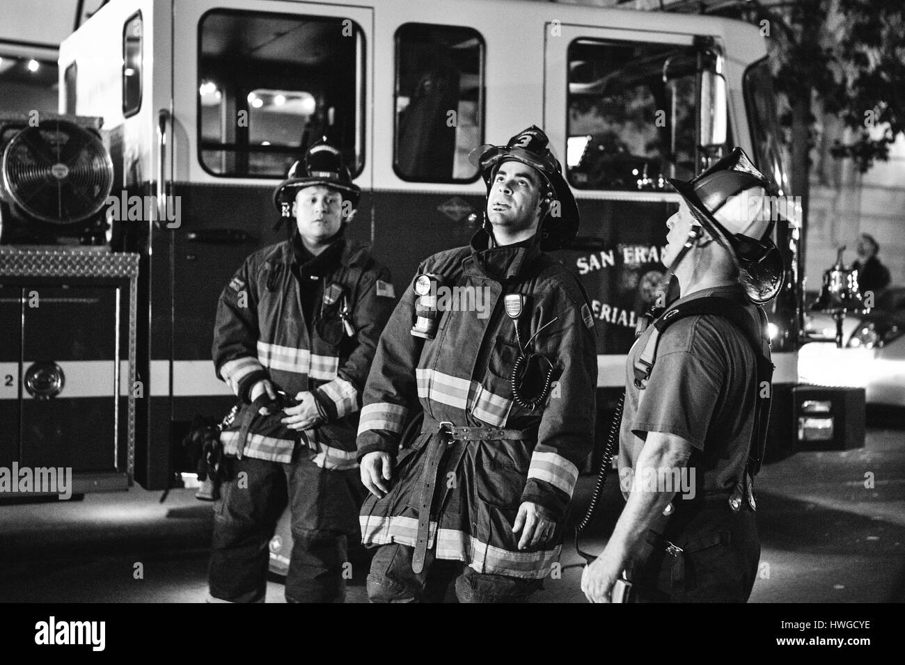 Drei Feuerwehrleute stehen und sprechen durch ihre Feuerwehrauto. Stockfoto