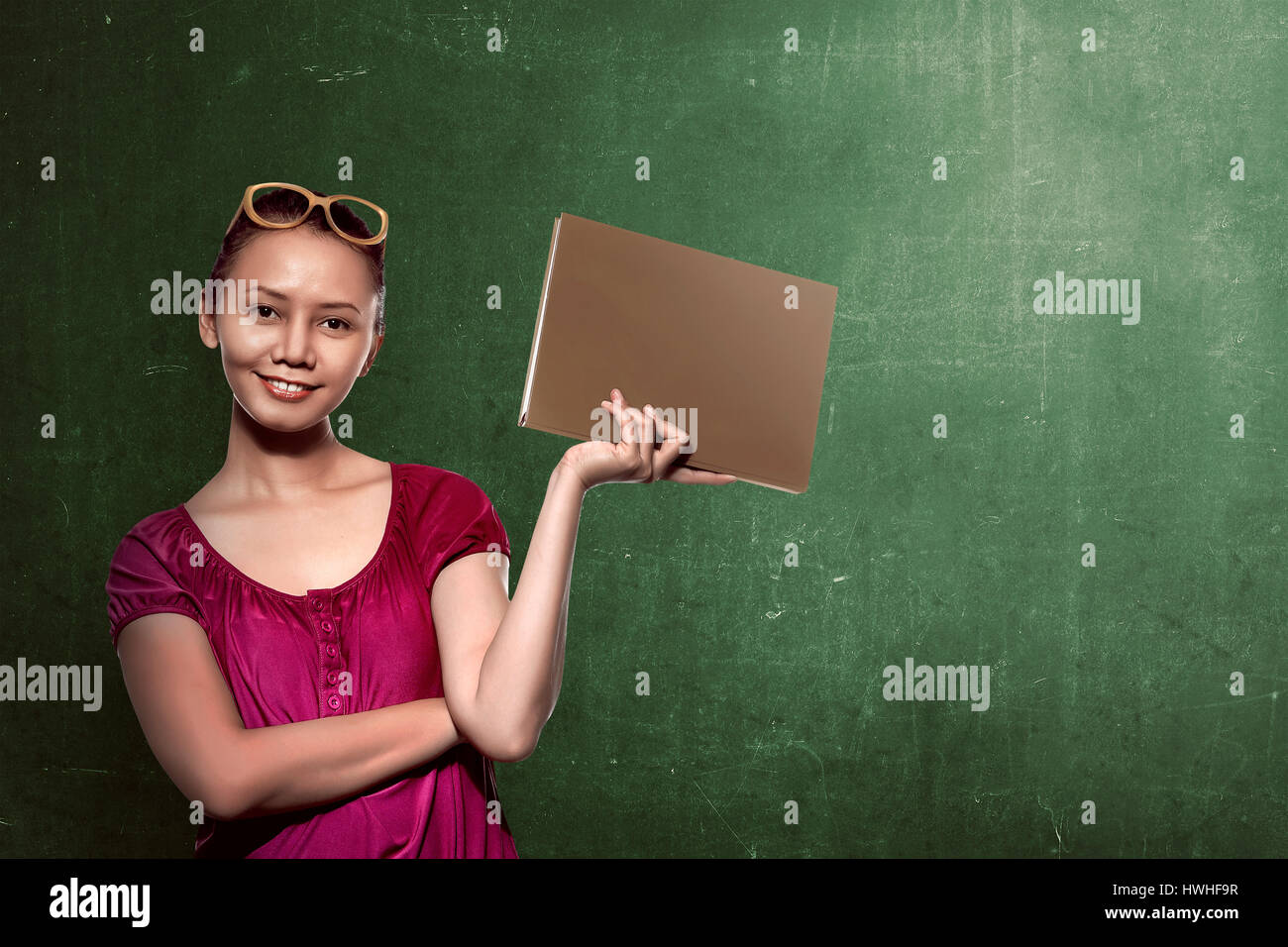 Asiatische Studentin Buch mit Tafel Hintergrund hält. Sie können Ihr Design auf dem Brett setzen. Stockfoto