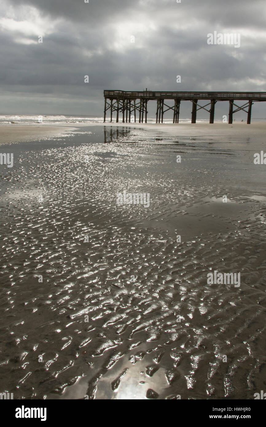 Farblos-Szene des Wassers im Sand kleine Wellen mit Steg und schwere Wolken im Hintergrund Stockfoto