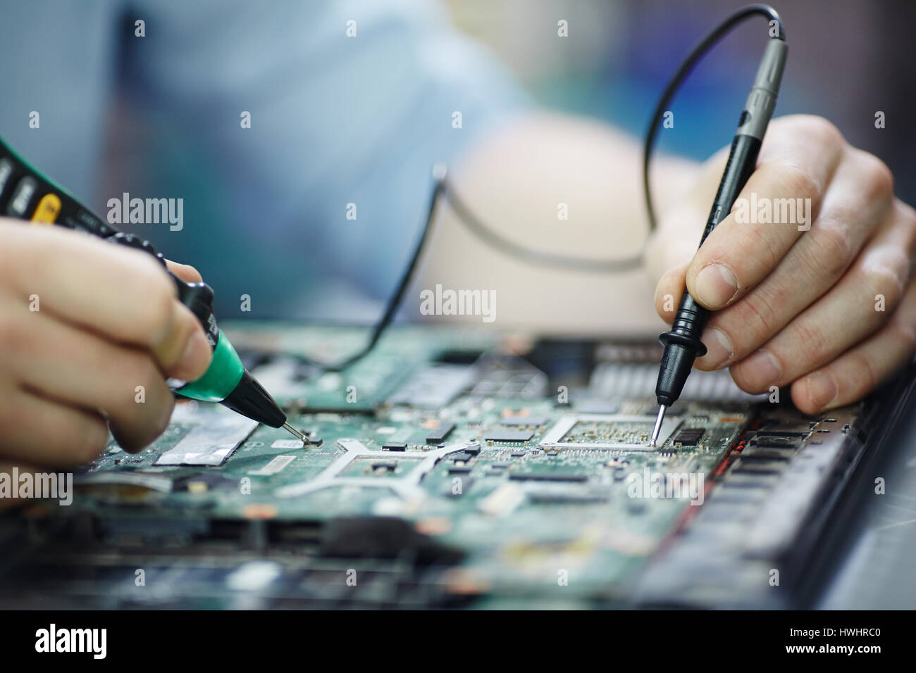 Closeup Aufnahme von männlichen Händen testen elektrischen Strom Spannung in Platine zerlegt Laptop mit multimeter Werkzeug auf Tabelle in Werkstatt Stockfoto