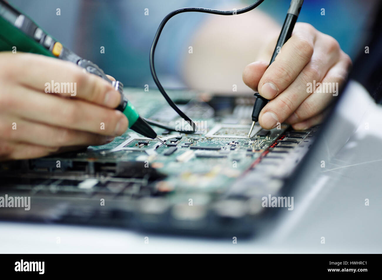 Closeup Aufnahme der Hände Prüfung elektrischen Strom in Platine zerlegt Laptop mit multimeter Werkzeug auf Tabelle in Werkstatt Stockfoto