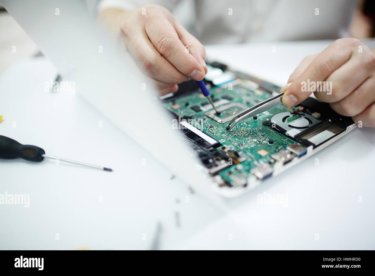 Closeup Aufnahme von männlichen Händen, die Reparatur von Teilen in zerlegt Laptop mit Schraubenzieher und verschiedene Werkzeuge auf Tisch in Werkstatt Stockfoto