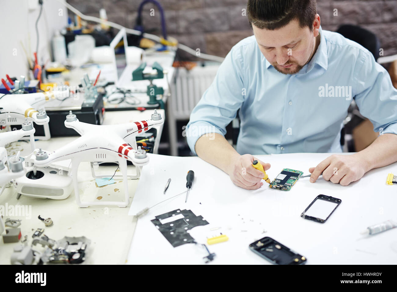 Hohen Winkel Schuss des modernen Menschen mobile Gerät auf Tisch mit verschiedenen disassemblierten Elektronik, Teile und Drohnen in modernen Werkstatt zu reparieren Stockfoto