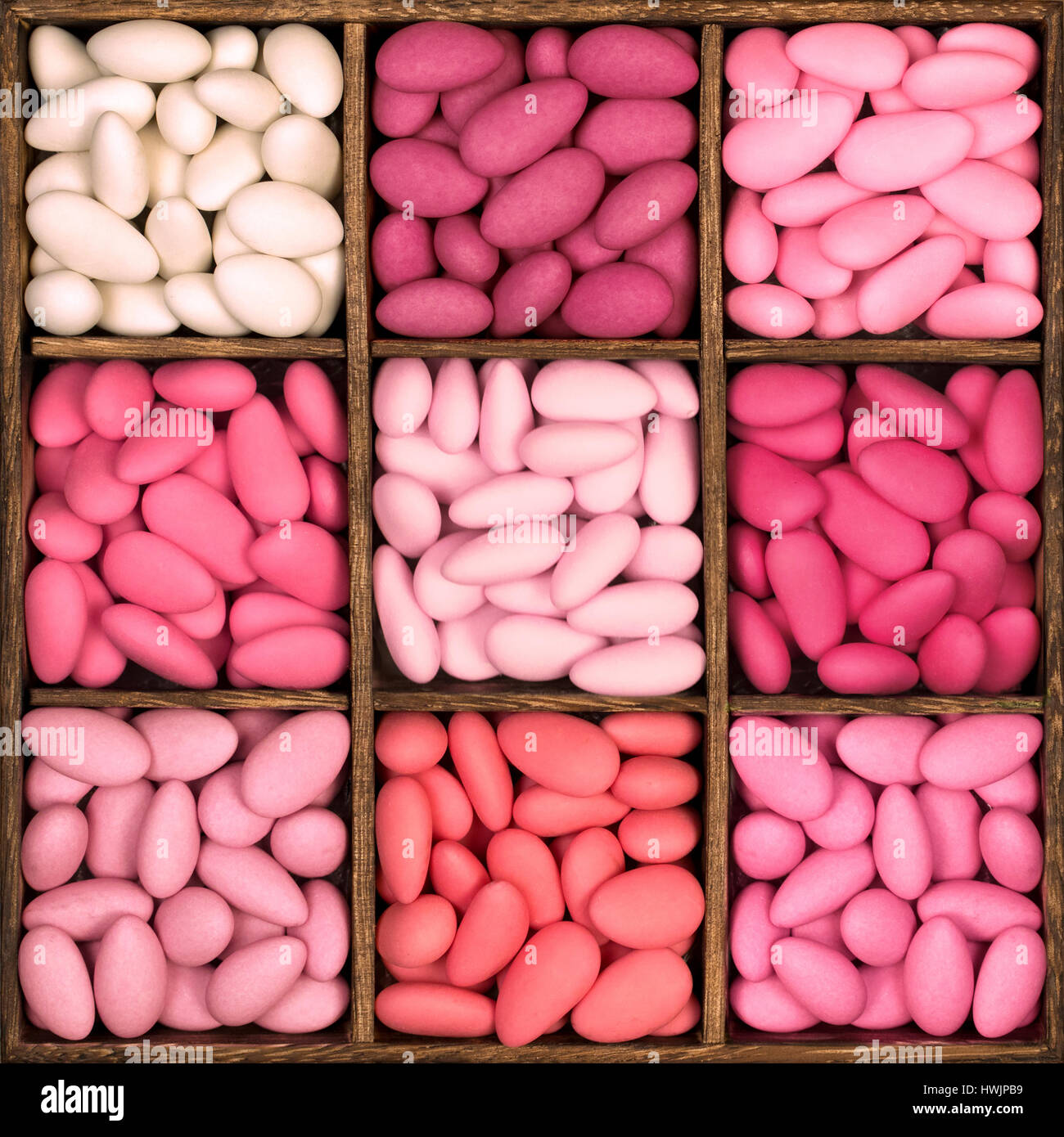 Hölzerne Aufbewahrungsbox mit neun Fächern, gefüllt mit einer Auswahl an Zuckermandeln in Schattierungen von rosa Quadrat. Diese bitter süßen Leckereien sind eine tradit Stockfoto