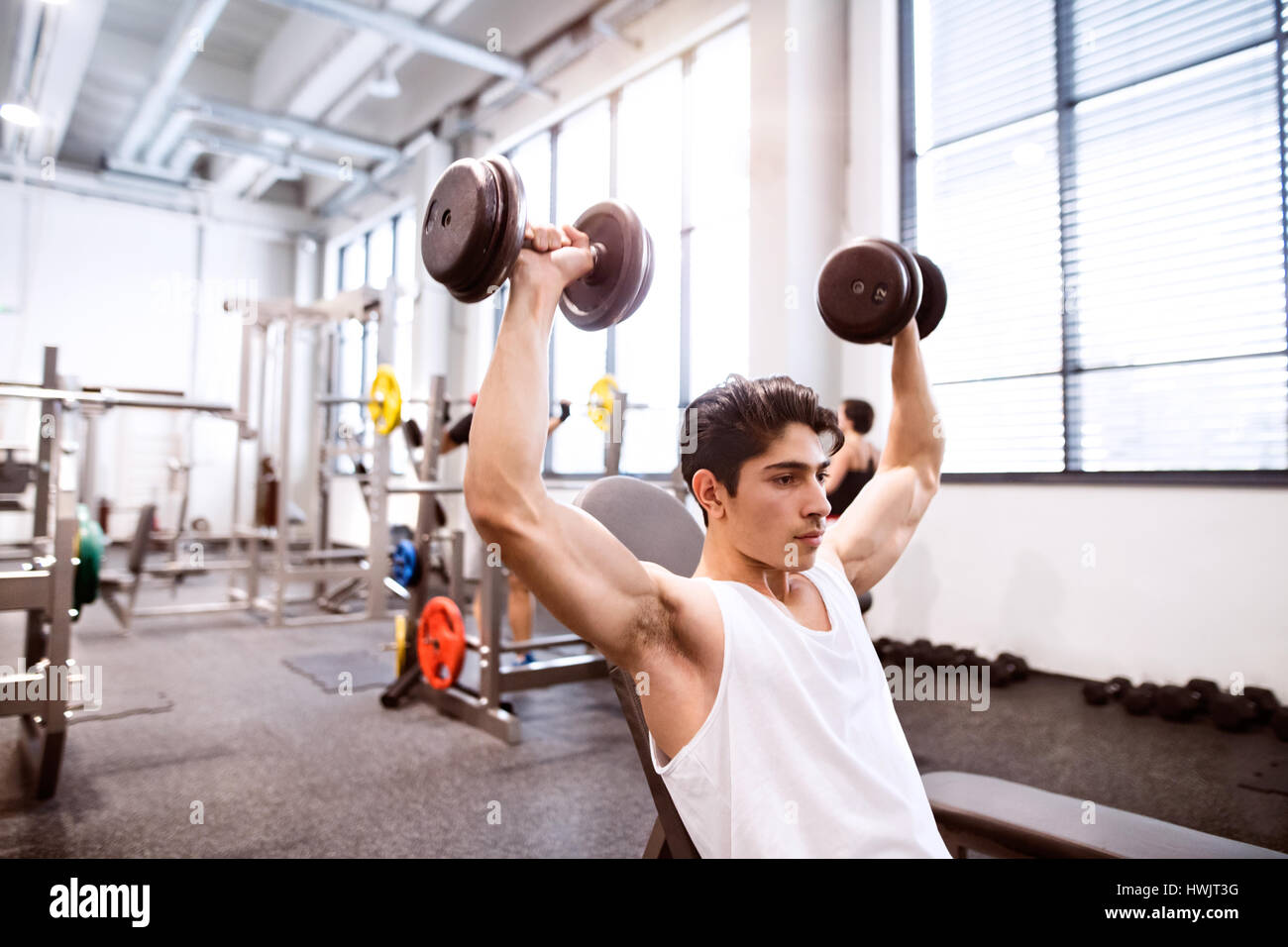 Junge spanische Fitness Mann in Turnhalle sitzen auf Bank, trainieren mit Gewichten Stockfoto