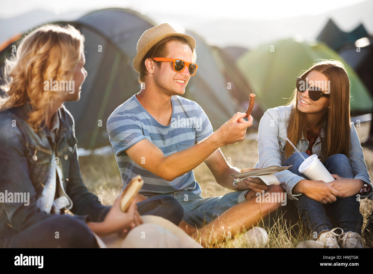 Gruppe von Teenager-Jungen und Mädchen im Sommer-Musikfestival, sitzen auf dem Boden vor Zelten Essen Stockfoto