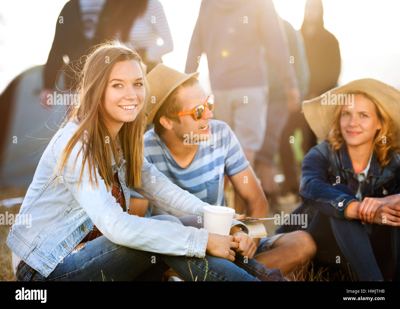 Gruppe von Teenager-Jungen und Mädchen im Sommer-Musikfestival, sitzen auf dem Boden vor Zelten, ausruhen und Essen Stockfoto
