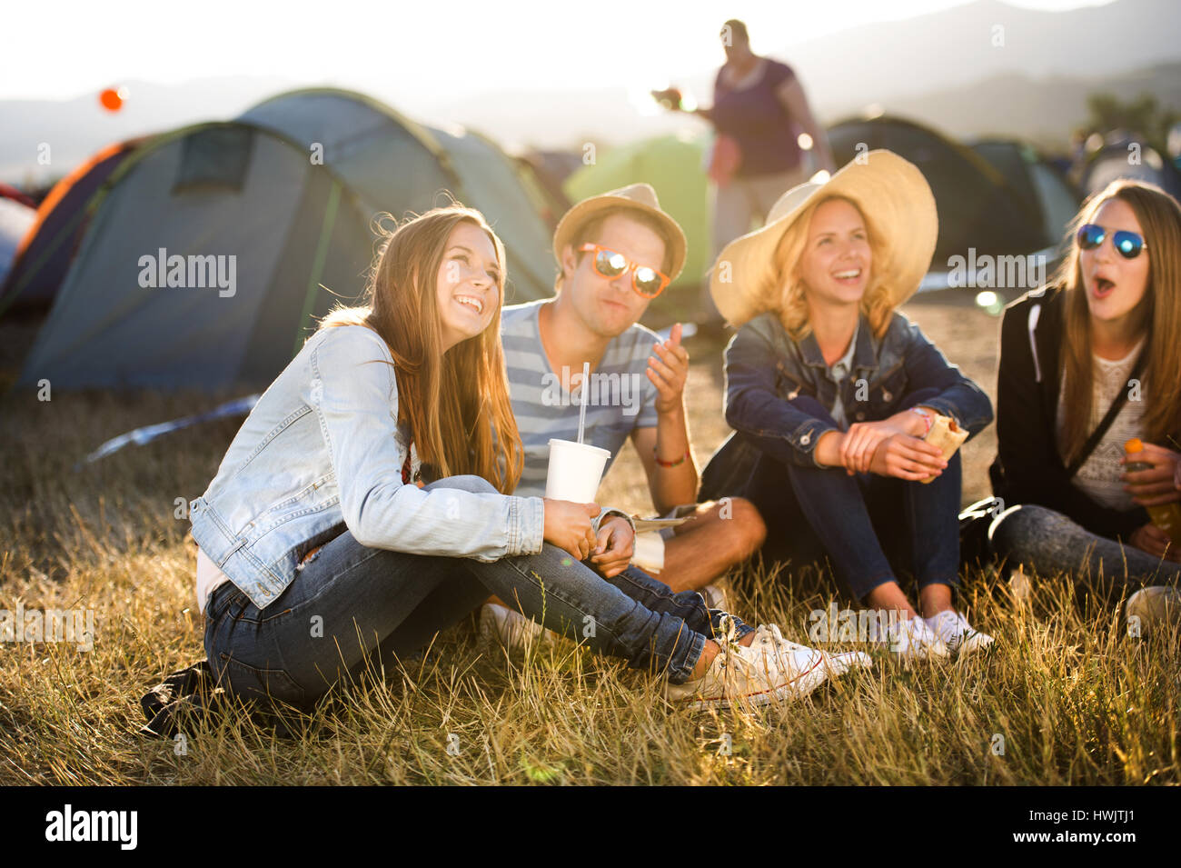 Gruppe von Teenager-Jungen und Mädchen im Sommer-Musikfestival, sitzen auf dem Boden vor Zelten Essen Stockfoto