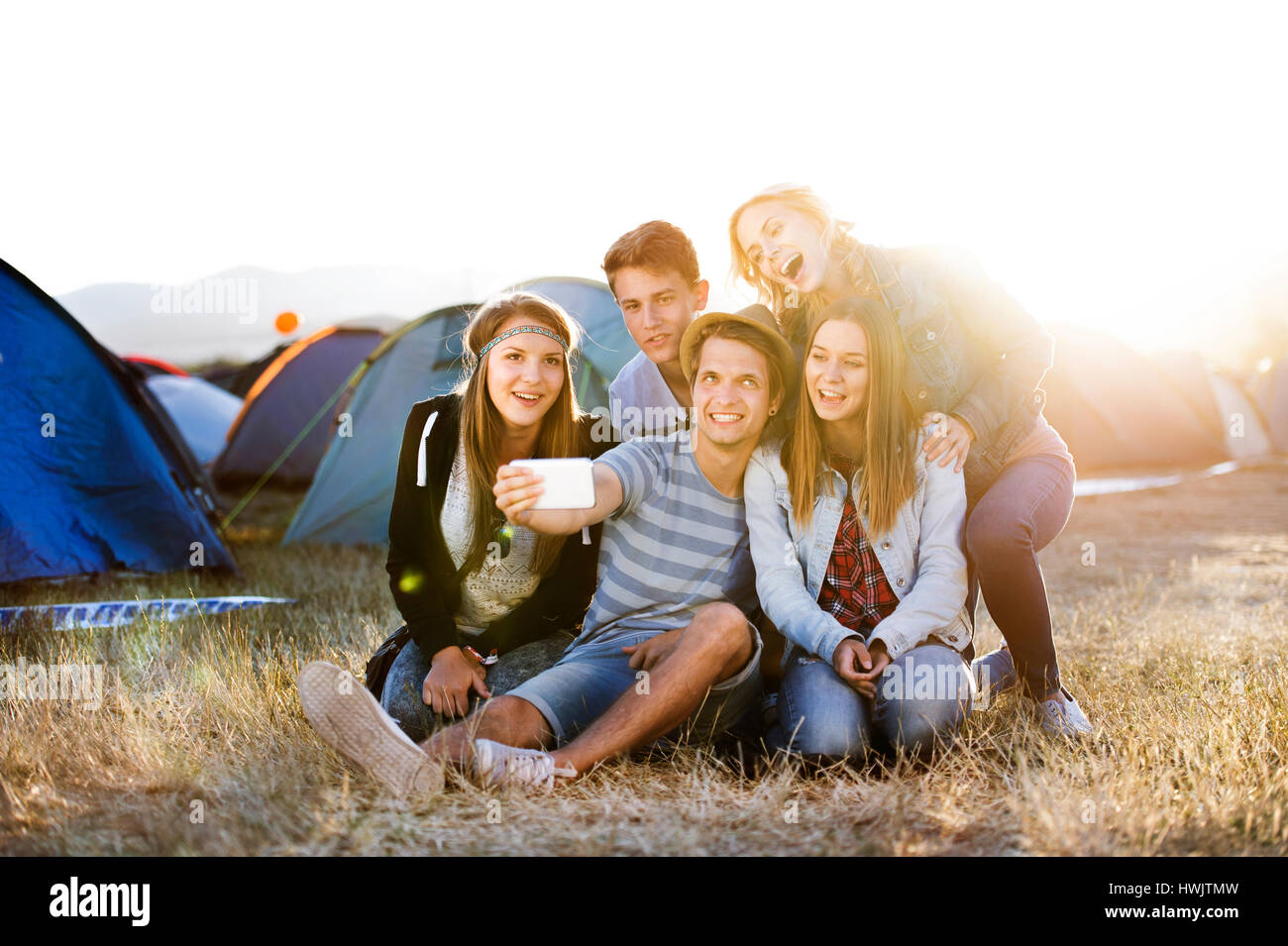 Gruppe von Teenager-Jungen und Mädchen im Sommer-Musik-Festival, auf dem Boden sitzend, die Selfie mit Smartphone Stockfoto