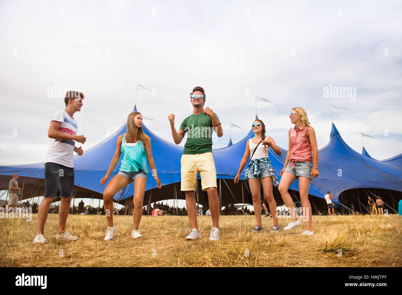 Gruppe von Teenager-Jungen und Mädchen im Sommer-Musikfestival, tanzen vor grossen Zelt, sonnigen Tag Stockfoto