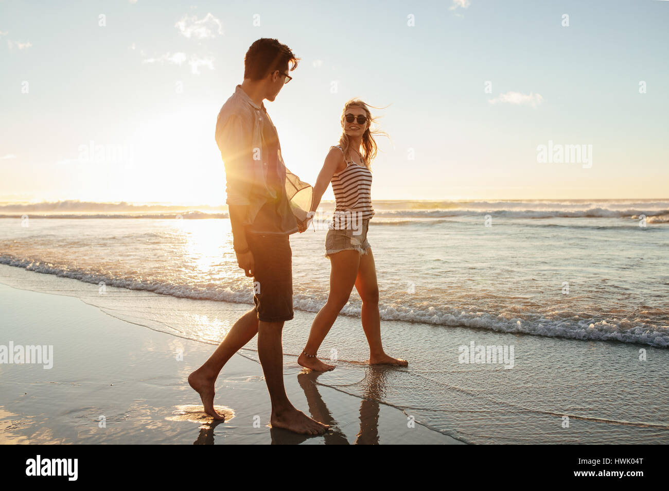 Im Freien Schuss romantischen jungen Paares zu Fuß entlang der Küste. Junger Mann und Frau zusammen spazieren am Strand bei Sonnenuntergang. Stockfoto