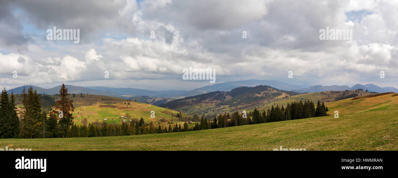 Frühling-Bergpanorama. Wolken und Sonne auf den Hügeln. Frühling-Sturm. April Regen. Dorf im Tal. April Ländliches Motiv Stockfoto