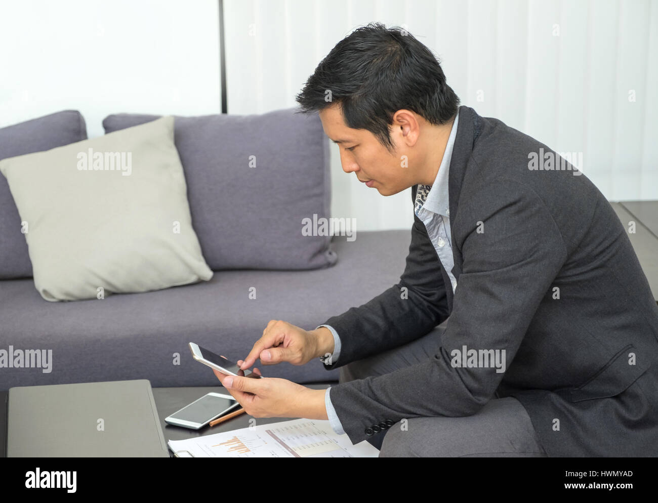 Geschäftsmann am Sofa sitzen und den Blick auf Handy-Bildschirm im Büro, Gefühl Stress über die Finanzkrise. Stockfoto