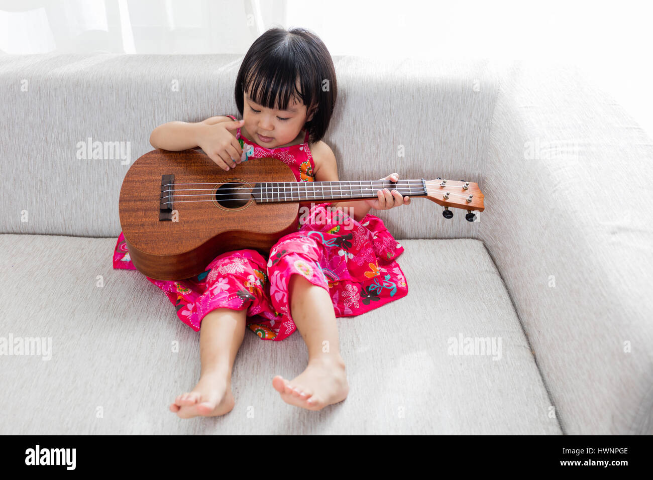 Asiatische chinesische Mädchen sitzt auf dem Sofa spielen Ukele. Stockfoto