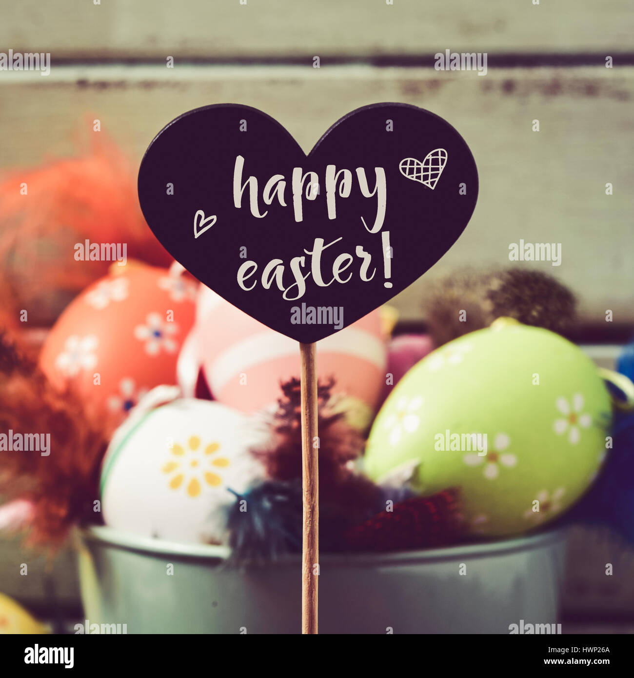 eine herzförmige schwarze Tafel mit dem Text Frohe Ostern geschrieben und Haufen von verschiedenen dekorierte Ostereier und Federn in verschiedenen Farben Stockfoto