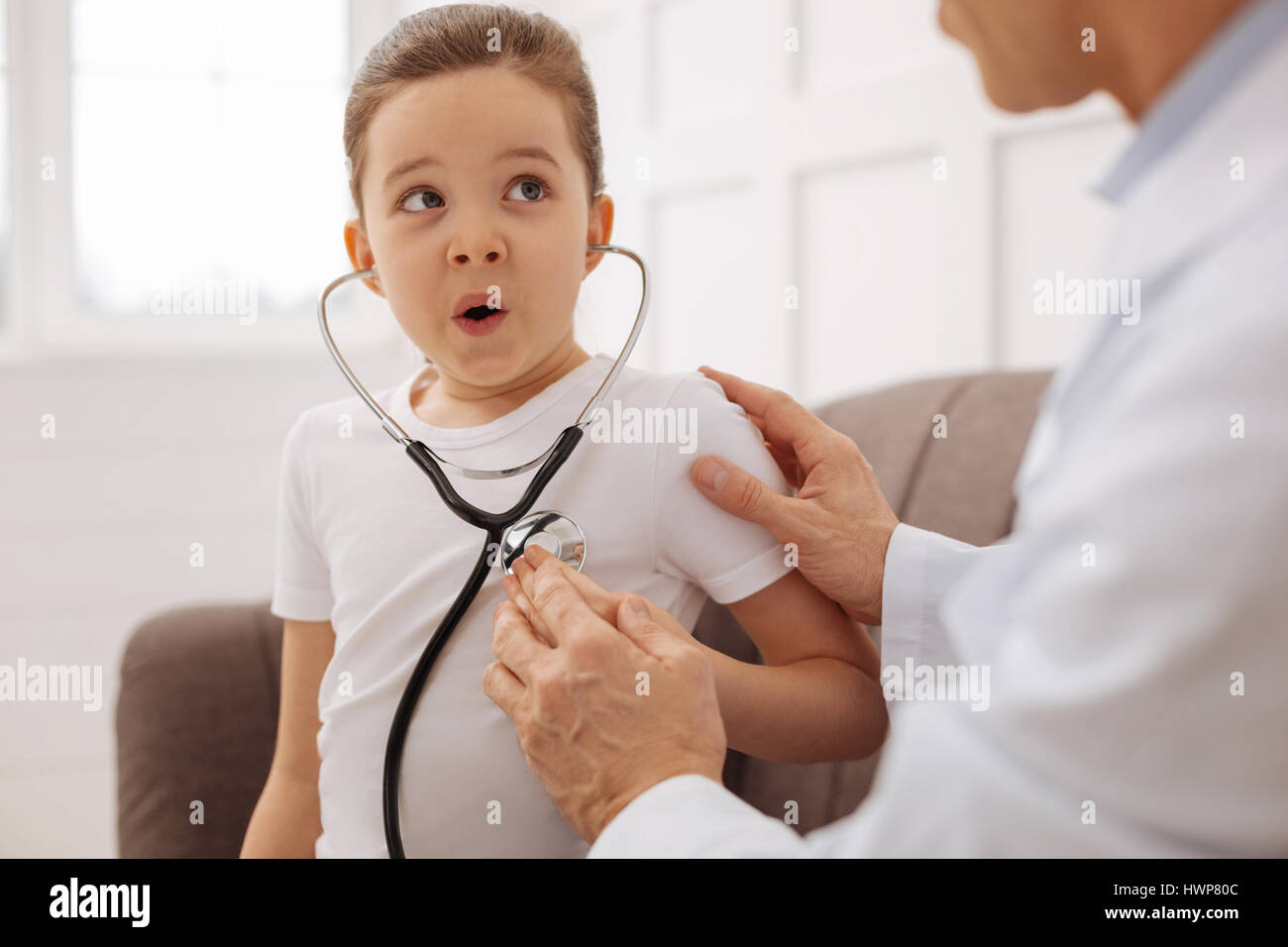 Ich kann es hören. Professionelle schöne aufmerksamen Kinderarzt unterhaltsam sein Patient mit seinem Stethoskop machen das Mädchen ihren Herzschlag hören Stockfoto