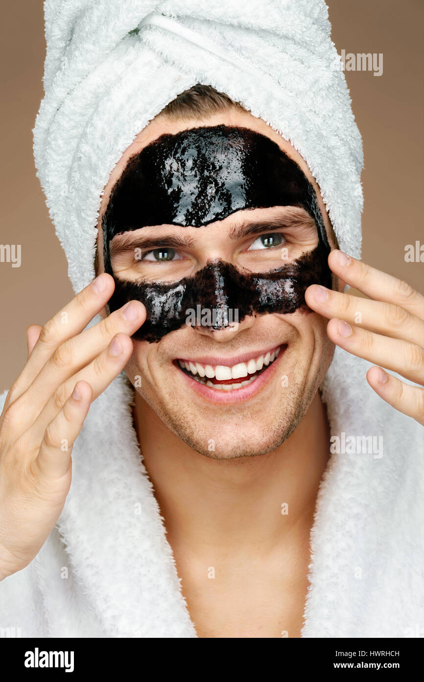 Glücklicher Mann mit schwarzer Maske auf dem Gesicht. Foto von gepflegten Mann Spa-Behandlungen erhalten. Schönheit & Skin care Konzept Stockfoto