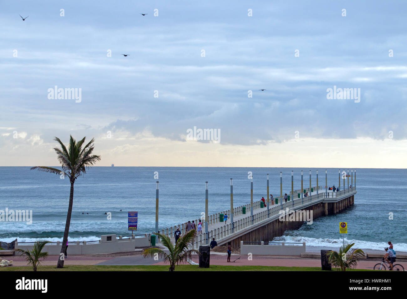 DURBAN, Südafrika - 23. März 2017: viele unbekannte am frühen Morgen Besucher am Strand und Pier gegen ruhige See und bewölkten blauen Skyline in Durban Stockfoto