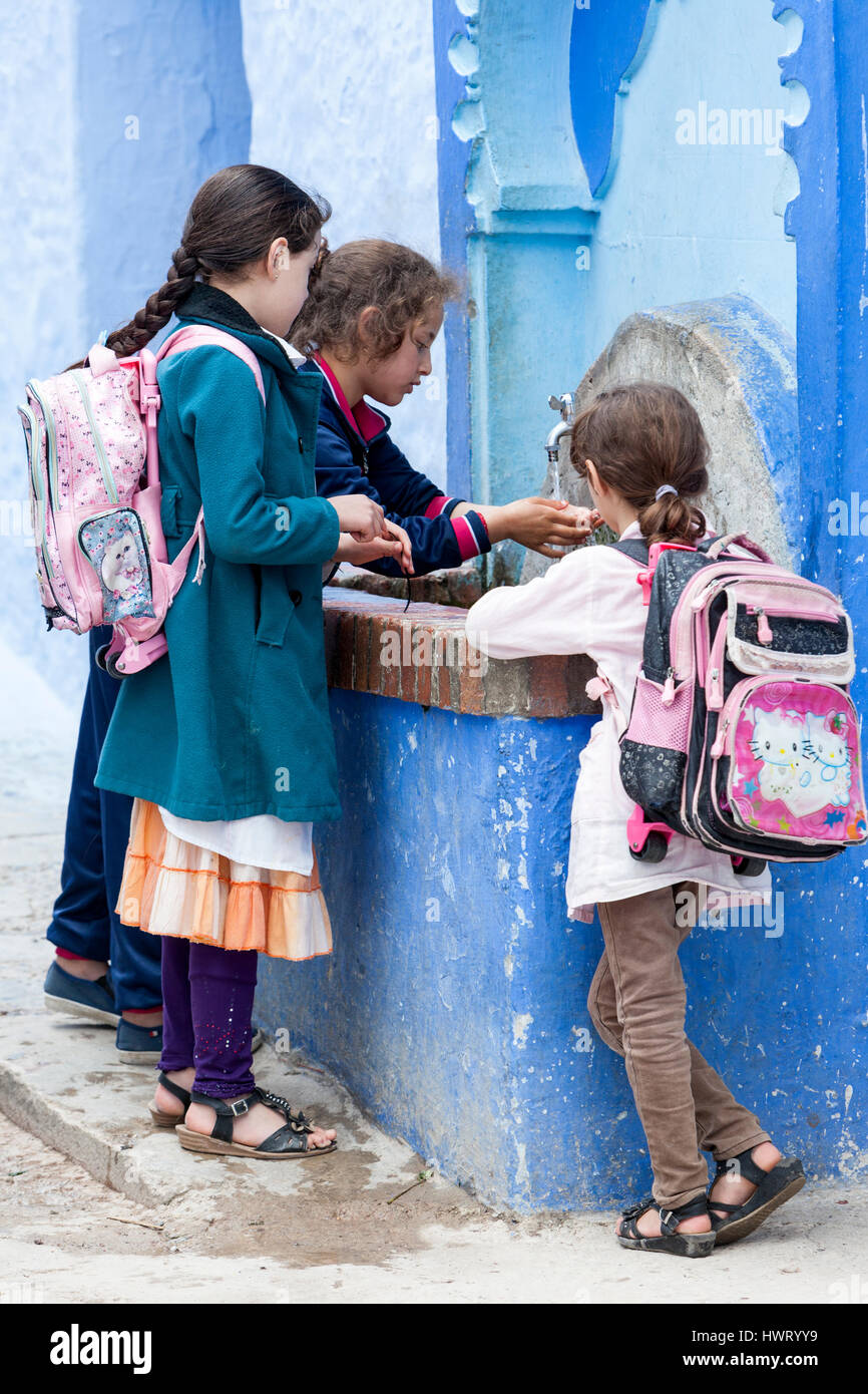 Chefchaouen, Marokko.  Junge Schulmädchen am öffentlichen Wasserhahn. Stockfoto