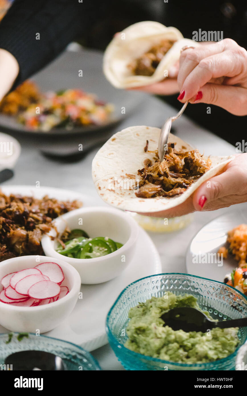 Hand der Frau bereitet Taco mit Freund am Esstisch sitzend beschnitten Stockfoto