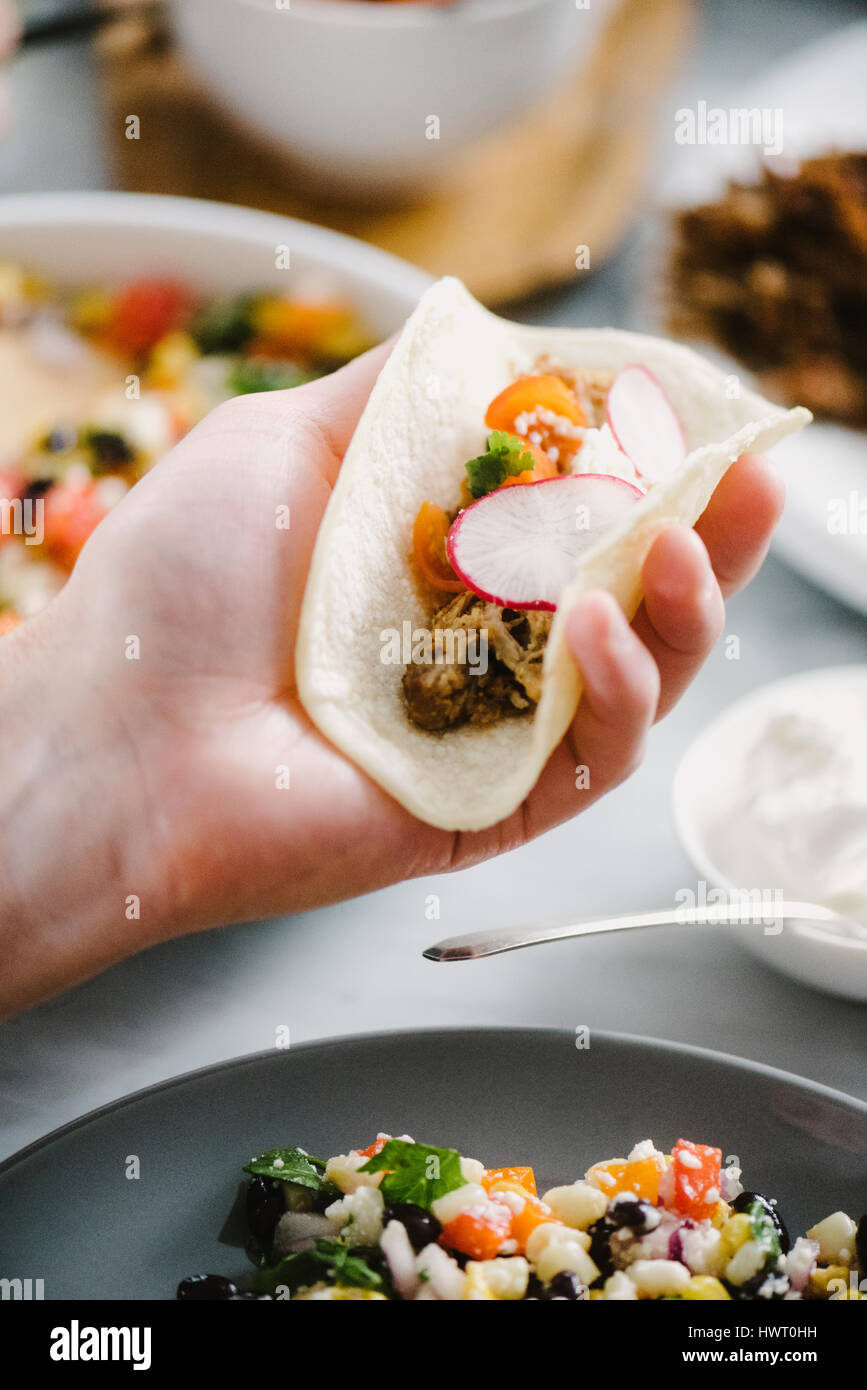 Abgeschnitten von Menschenhand hält Taco am Esstisch Stockfoto