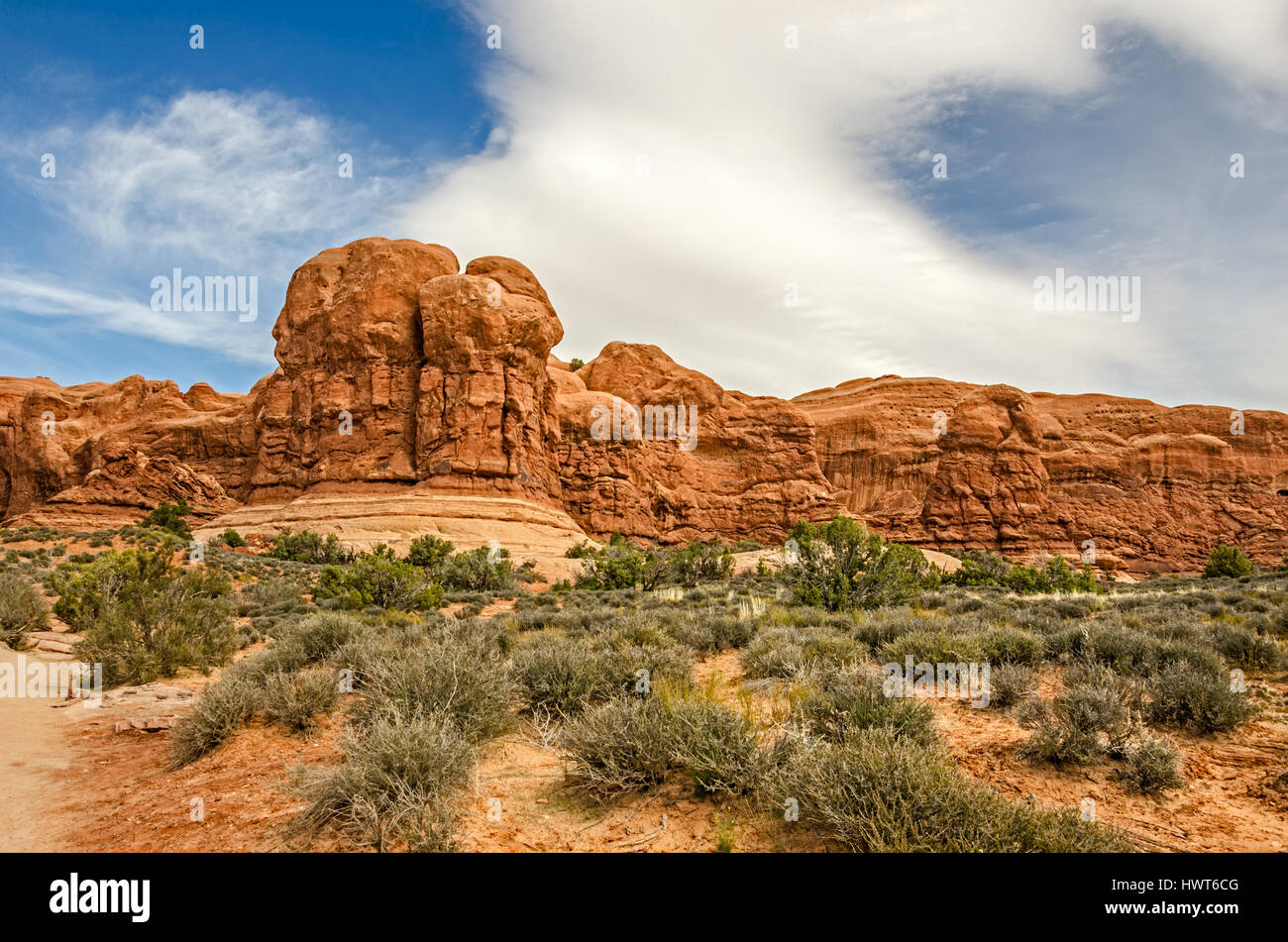 Schöne rote Sandstein Felsformationen werden durch interessante Wolkenformationen im Arches National Park in Utah hervorgehoben.  Grüne Sträucher bieten eine schöne Stockfoto