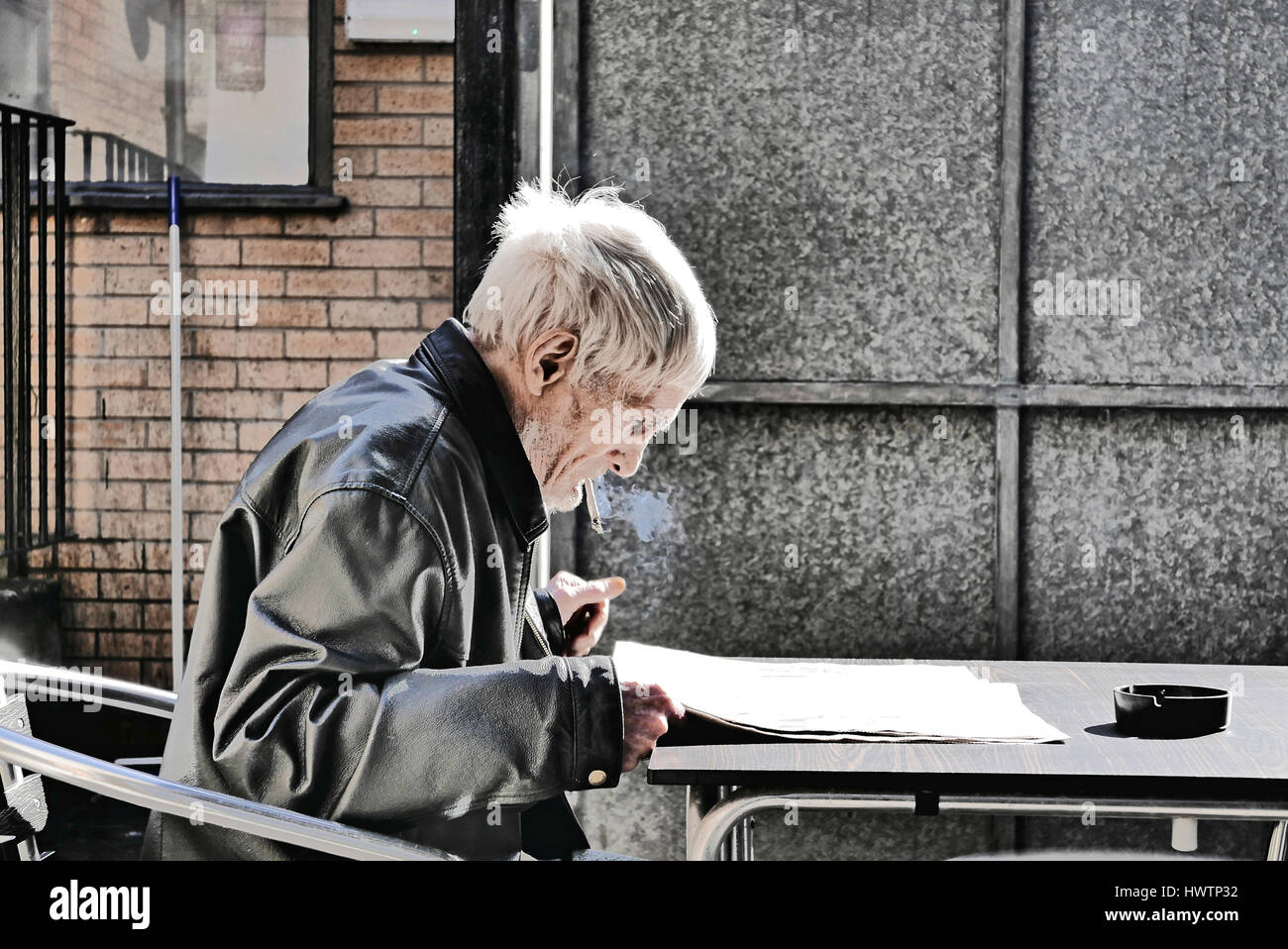 Senior woman in Lederjacke saß draußen rauchen und Zeitung lesen Stockfoto