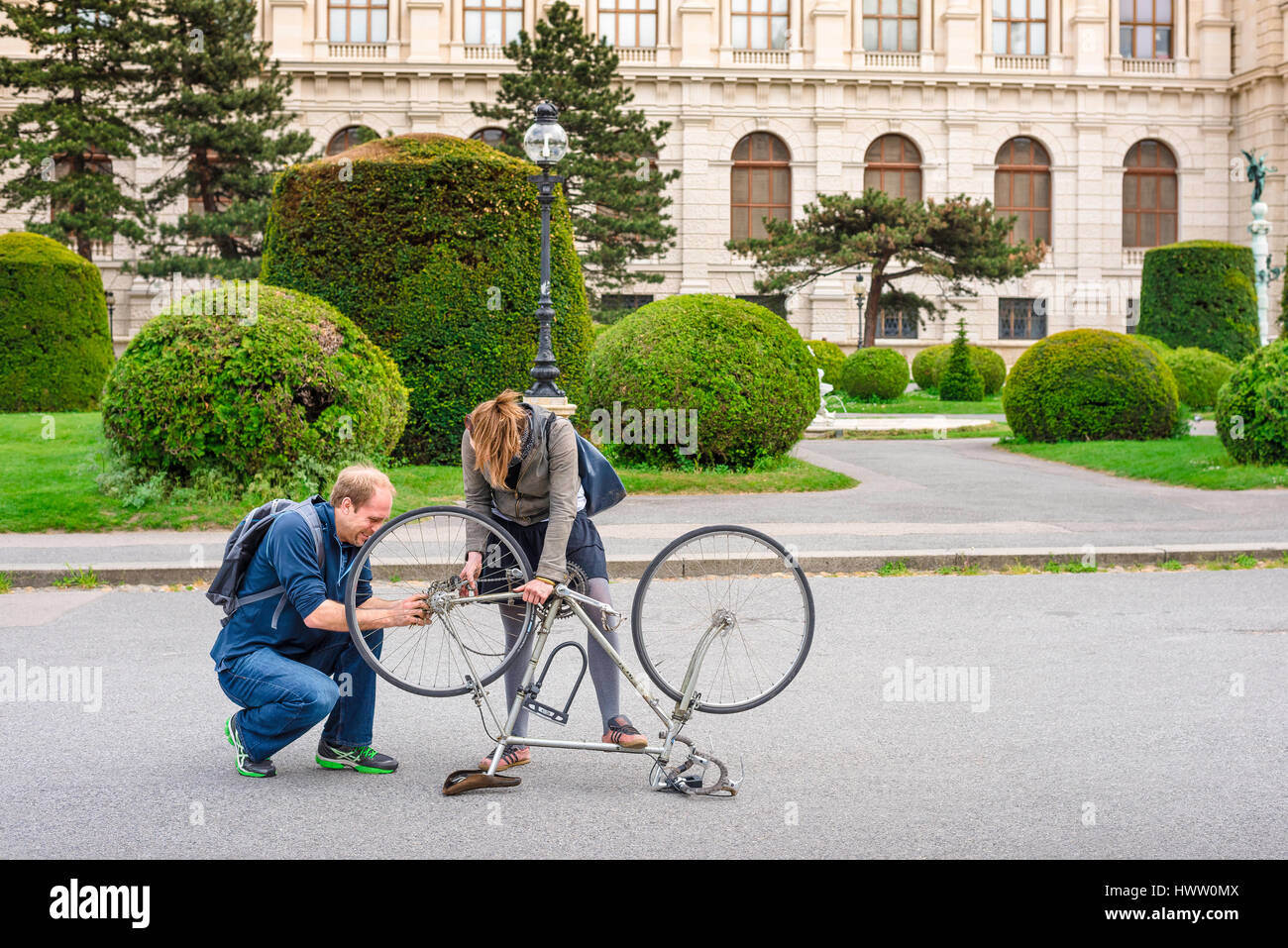 Helfende Hand, Blick auf einen jungen Mann und eine Frau, die zusammen an der Reparatur eines Fahrrads in Maria Theresienplatz, Wien, Österreich, arbeiten. Stockfoto