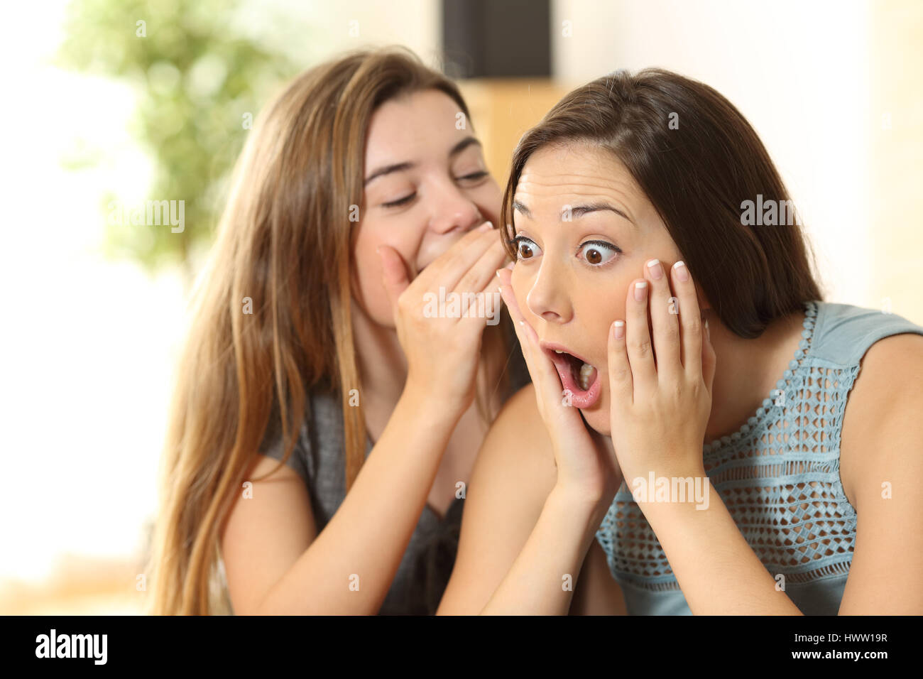 Porträt eines Mädchens erzählen Geheimnisse erstaunt Freundin sitzen auf einer Couch im Wohnzimmer zu Hause Stockfoto